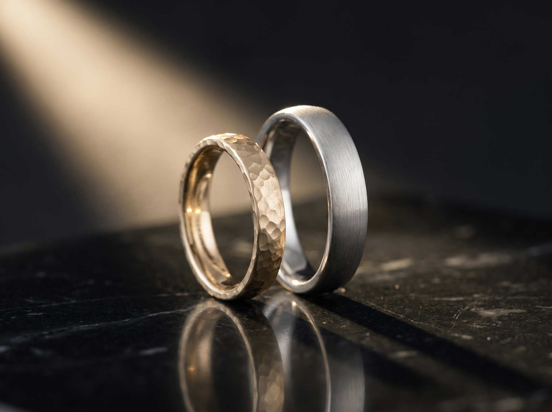 Zwei Trauringe aus Gold und Platin auf schwarzem Marmor